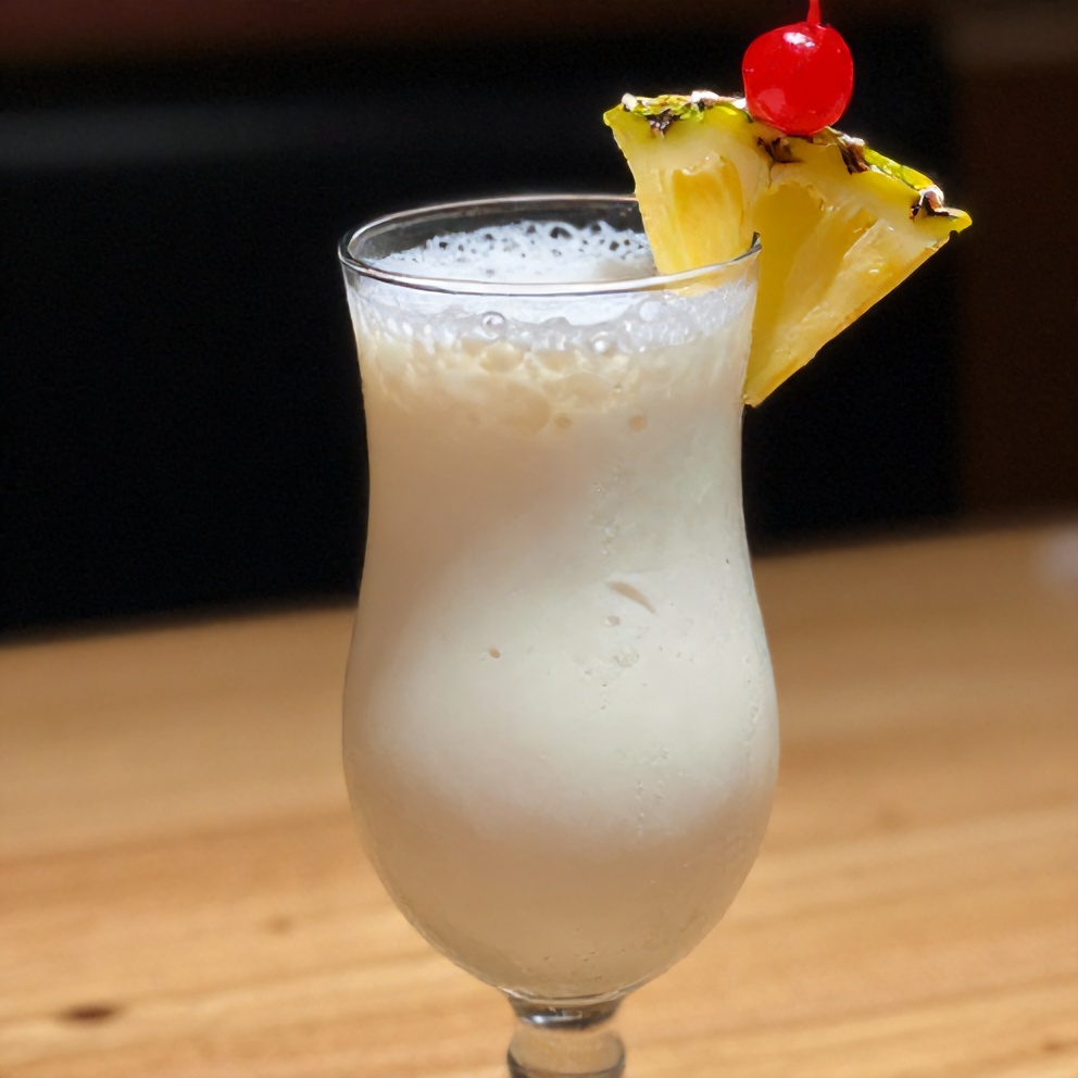 A close-up of a tall glass filled with a creamy coconut cocktail, garnished with a pineapple wedge and a cherry, sitting on a light wooden surface with warm side lighting highlighting the texture.
